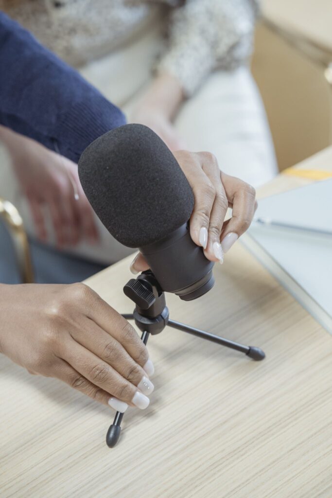 From above of crop anonymous female putting microphone on wooden table while recording podcast colleague in studio